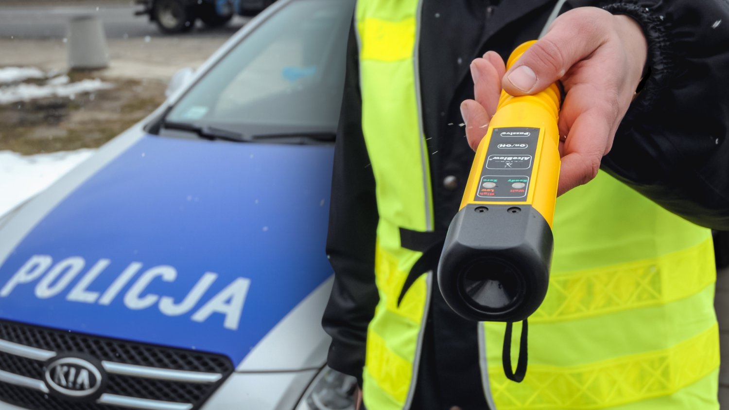 Policjant z alkomatem. W tle samochód policyjny