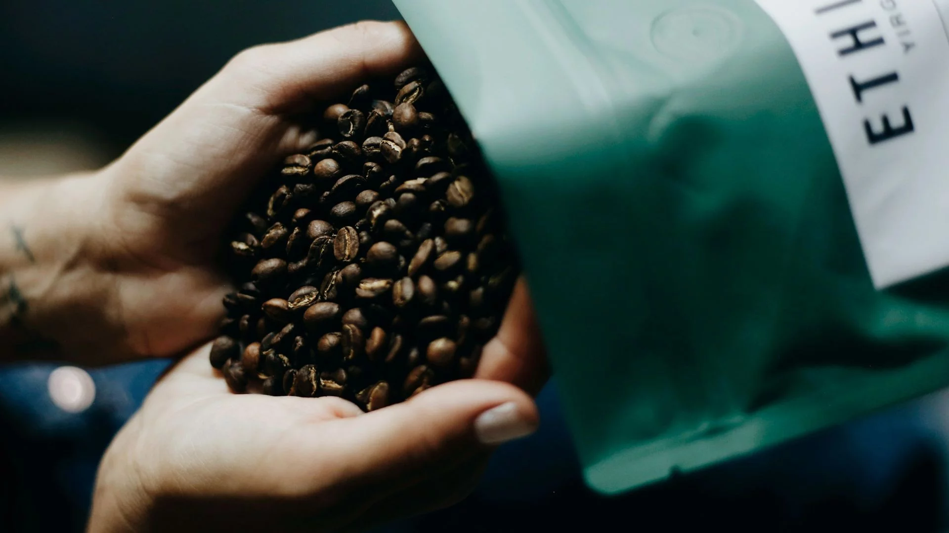 Ziarna kawy wysypywane z torebki na dłonie.