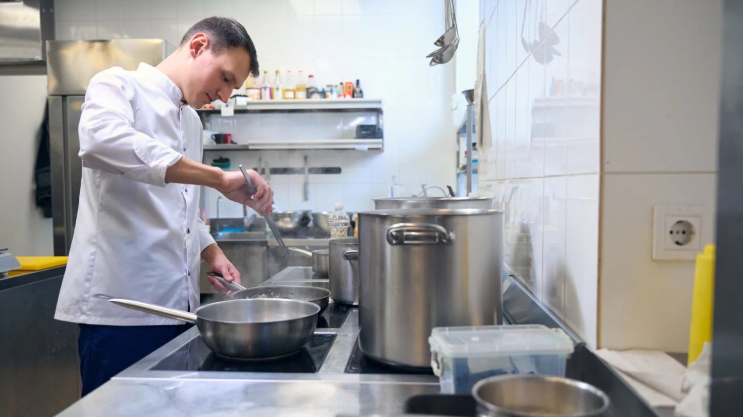 Polacy trzonem hoteli w Niemczech Młody kucharz smażący coś na patelni w dużej kuchni restauracyjnej