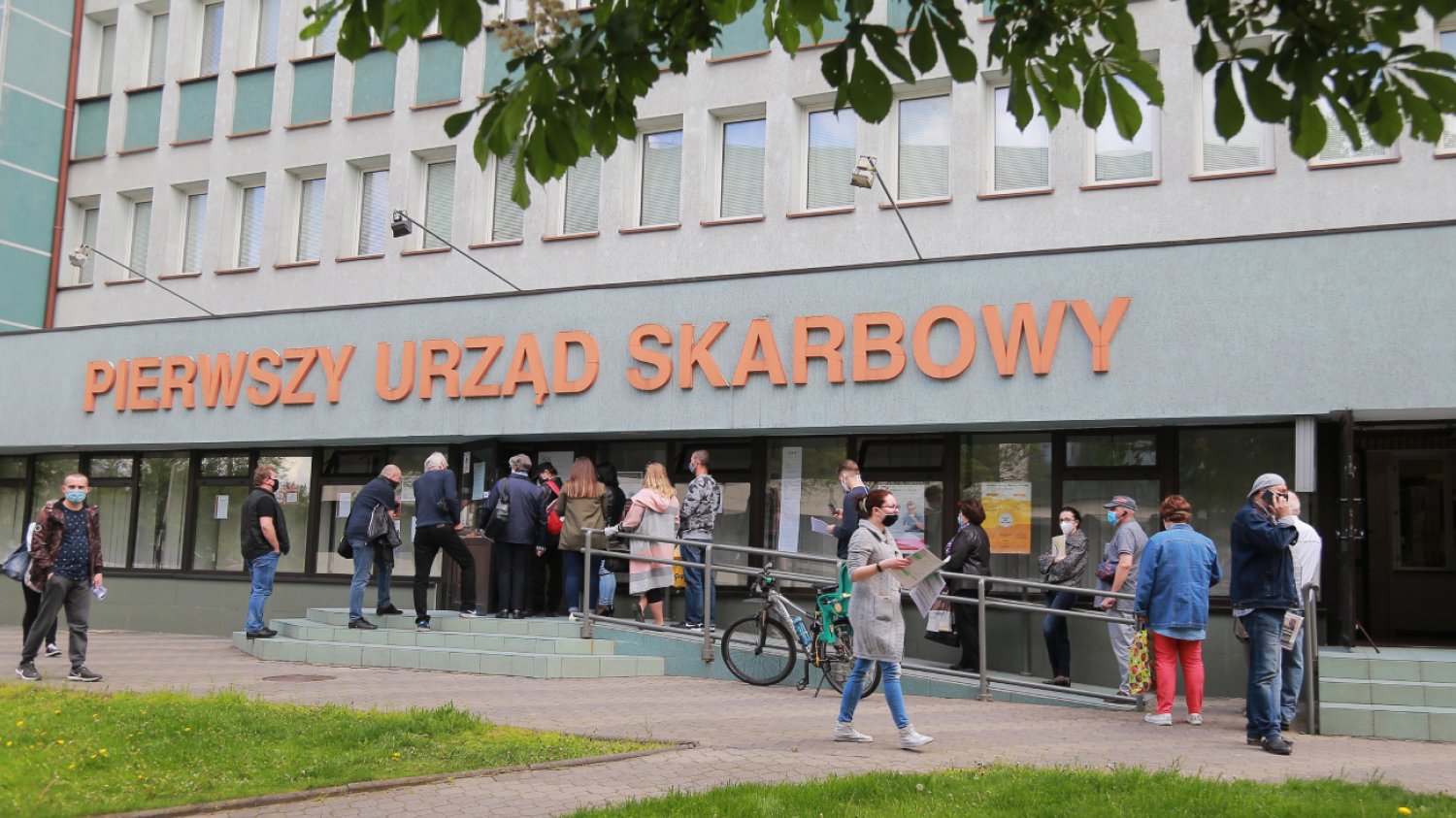 Kolejka do składania zeznań PIT przed wejściem do urzędu skarbowego. Na budynku wielki napis "pierwszy urząd skarbowy".