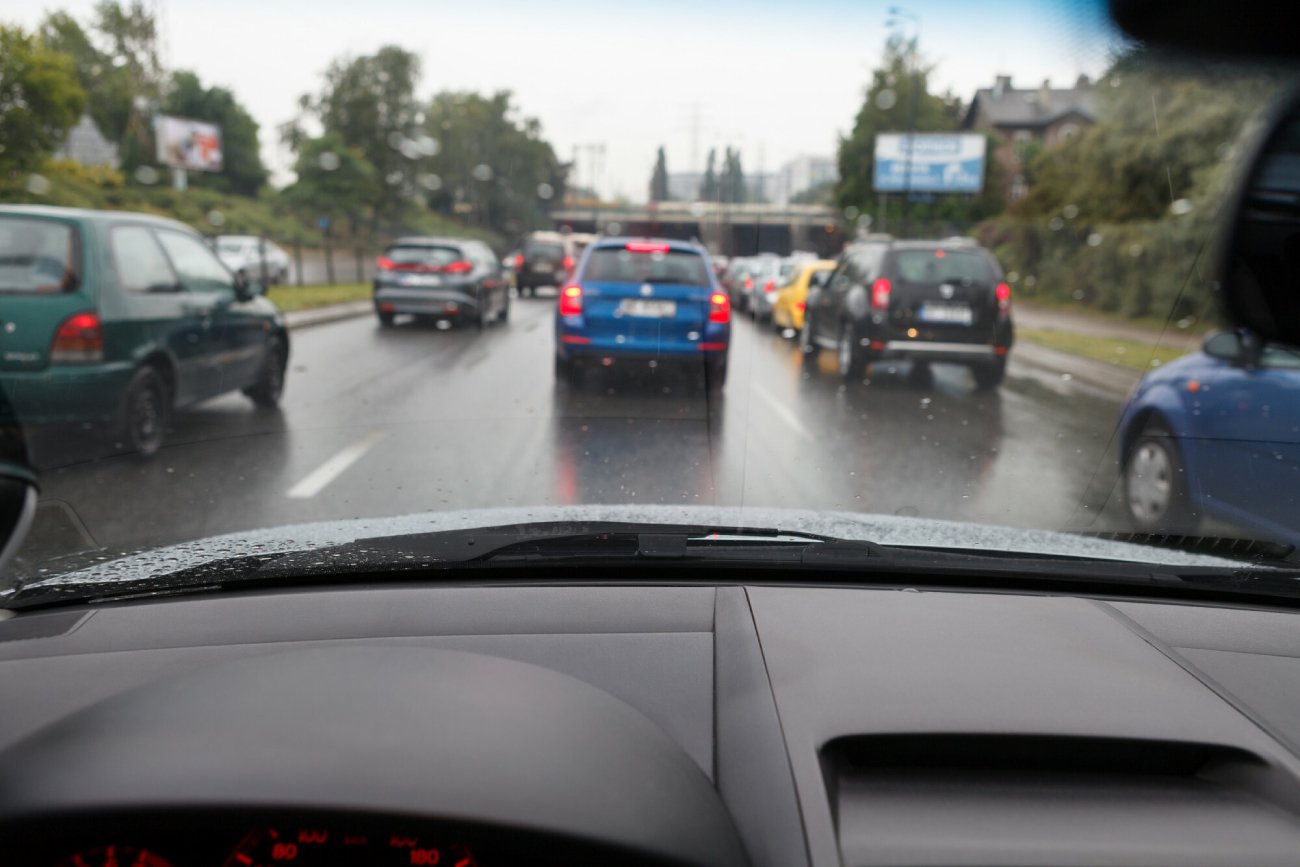 Auta odjeżdżające do pracy stoją w korku i pada na nie deszcz