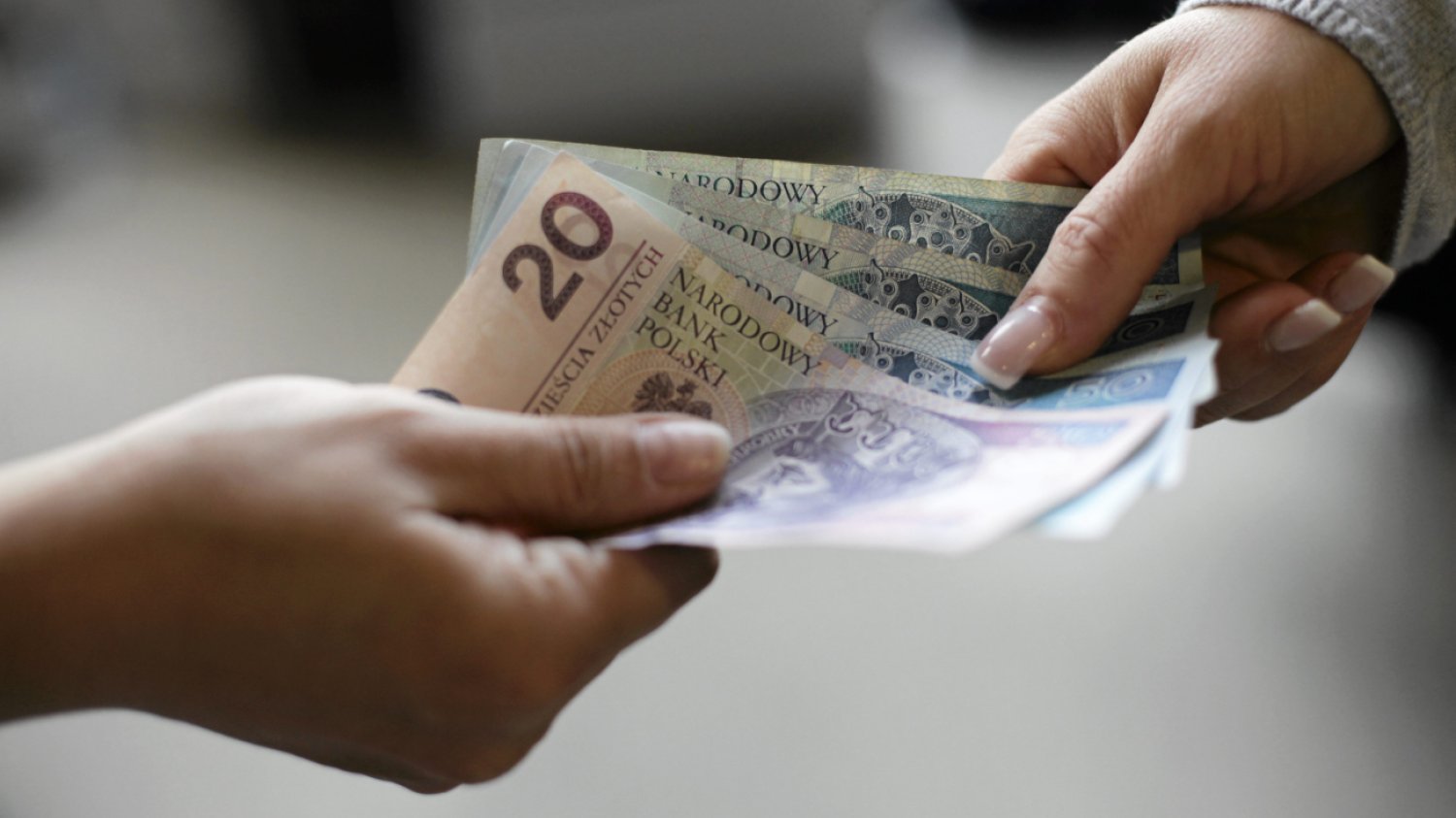 Ręce dwóch osób: jedna podaje drugiej kilkaset złotych w banknotach.