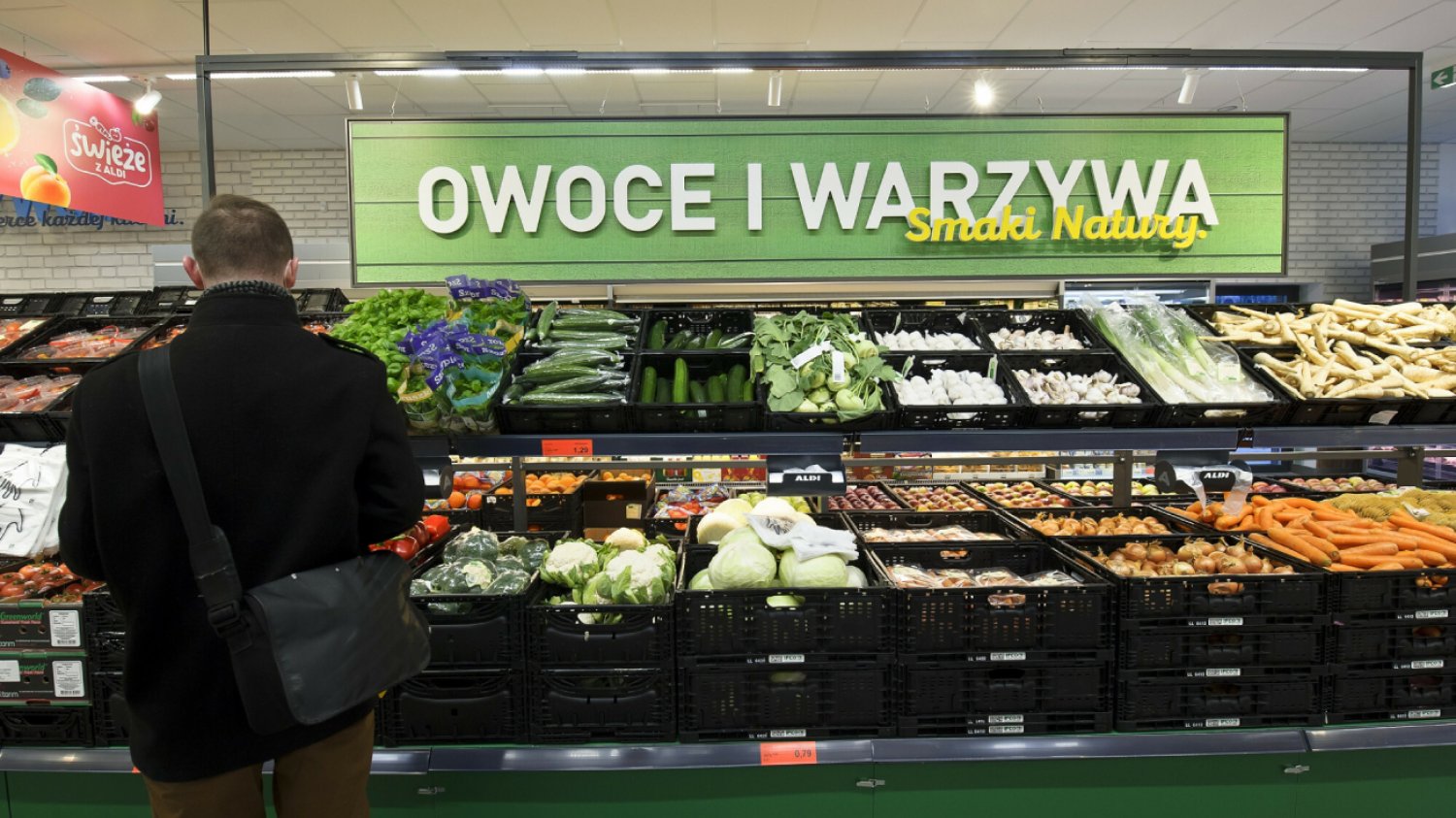 mężczyzna w czarnej kurtce robi zakupy na stoisku warzywa i owoce