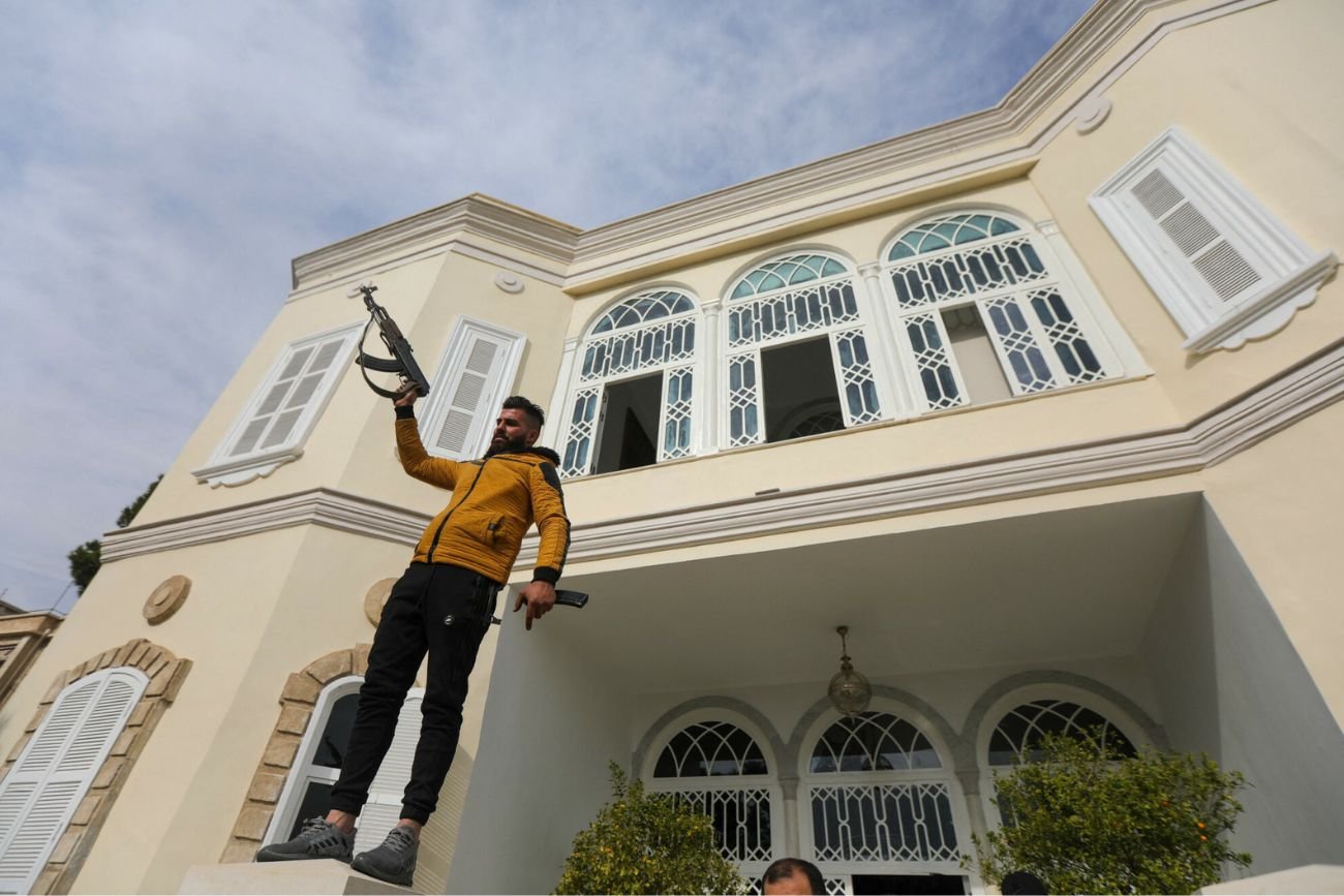 Jeden z bojowników sił opozycji świętuje przed wejściem do rezydencji Baszara al-Assada.