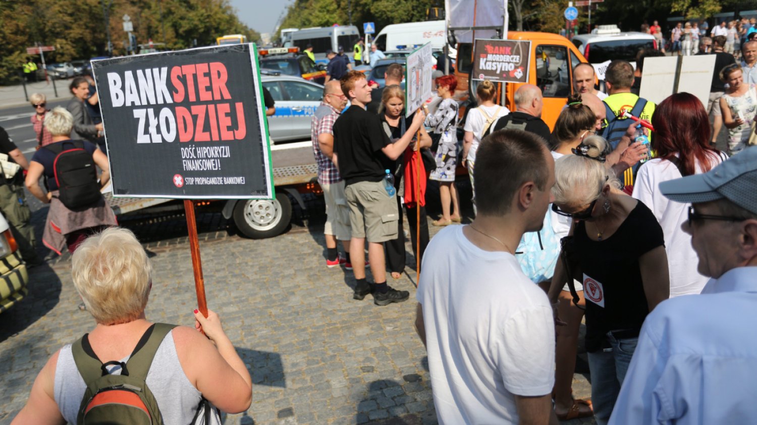 Grupa osób protestujących przeciwko kredytom we frankach szwajcarskich. Widoczny jest transparent z napisem "bankster złodziej".