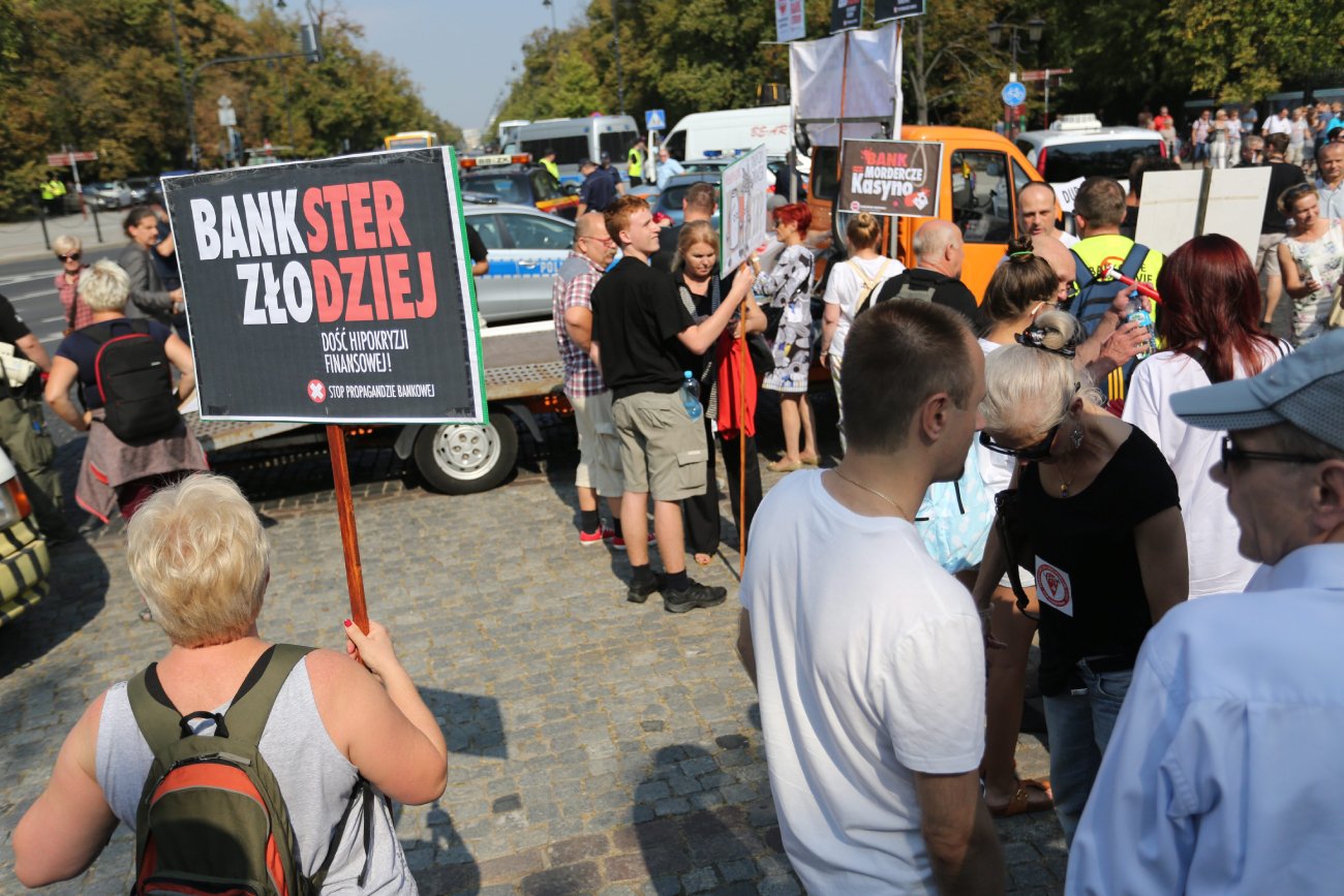 Grupa osób protestujących przeciwko kredytom we frankach szwajcarskich. Widoczny jest transparent z napisem "bankster złodziej".