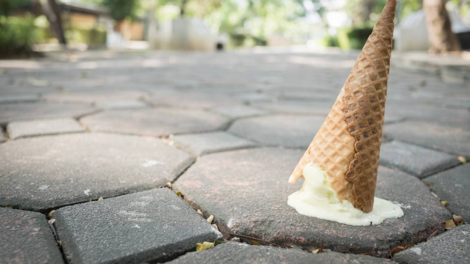 Lody upuszczone na chodnik. Zbliżenie na roztapiający się rożek i kostkę brukową.