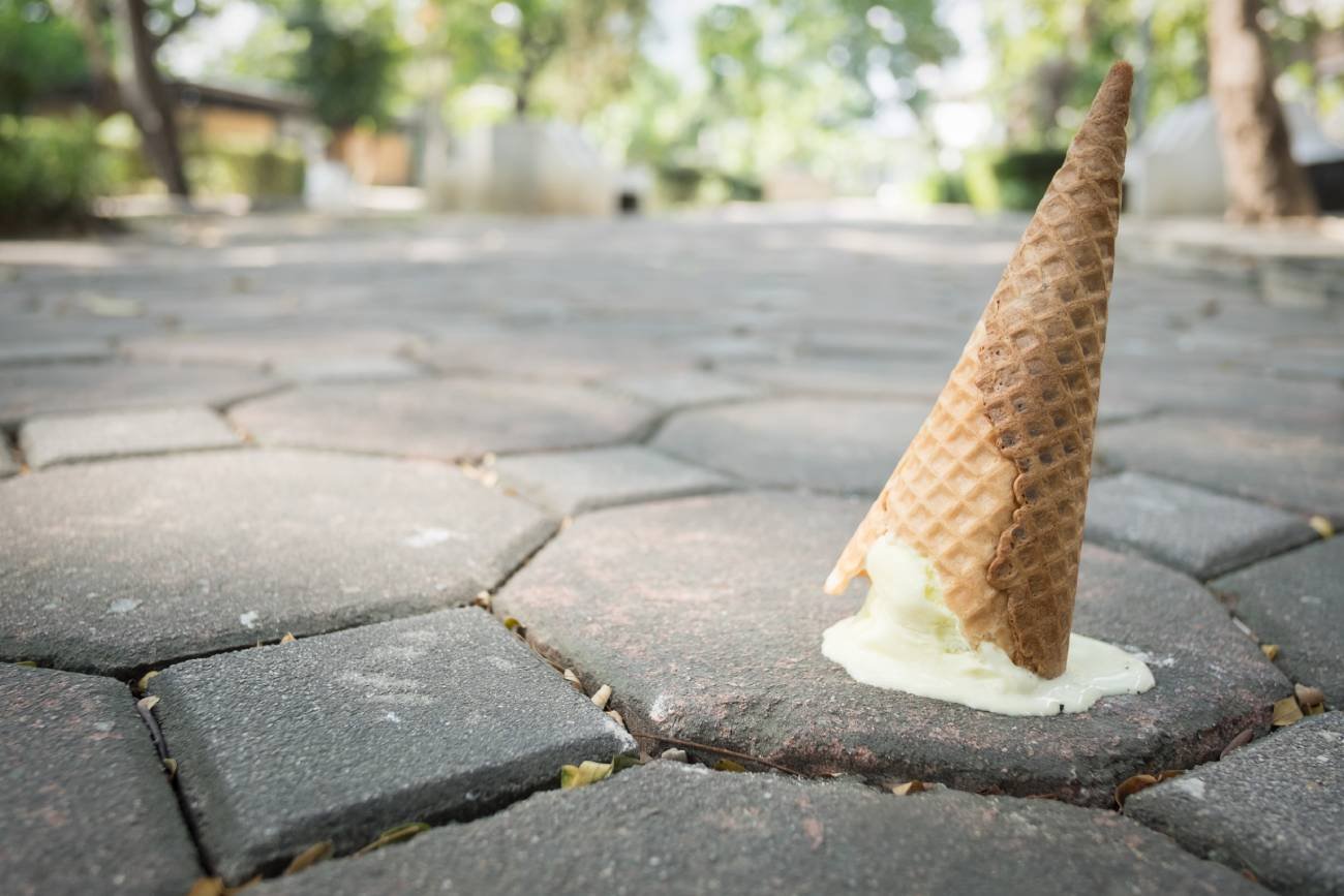 Lody upuszczone na chodnik. Zbliżenie na roztapiający się rożek i kostkę brukową.