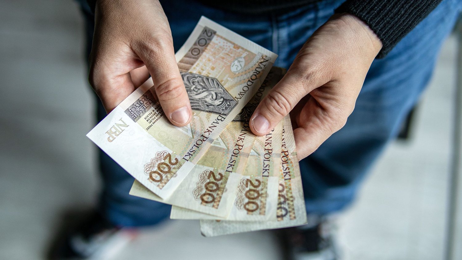Koniec bezwarunkowego 800 plus dla uchodźców. Pieniądze tylko za pracę mężczyzna trzymający banknoty 200-złotowe