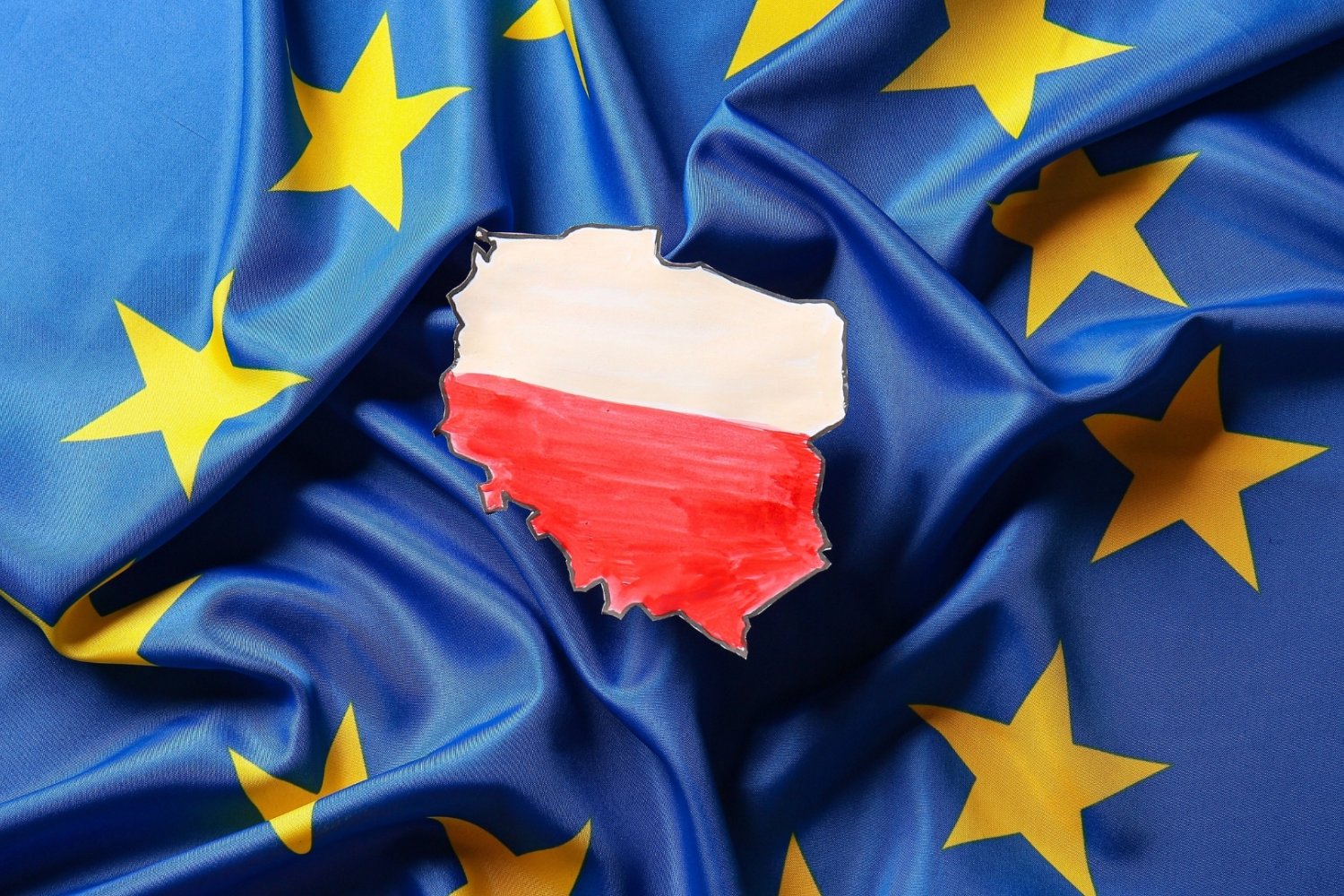 Flaga Polski w kształcie granic kraju. Leży na fladze Unii Europejskiej