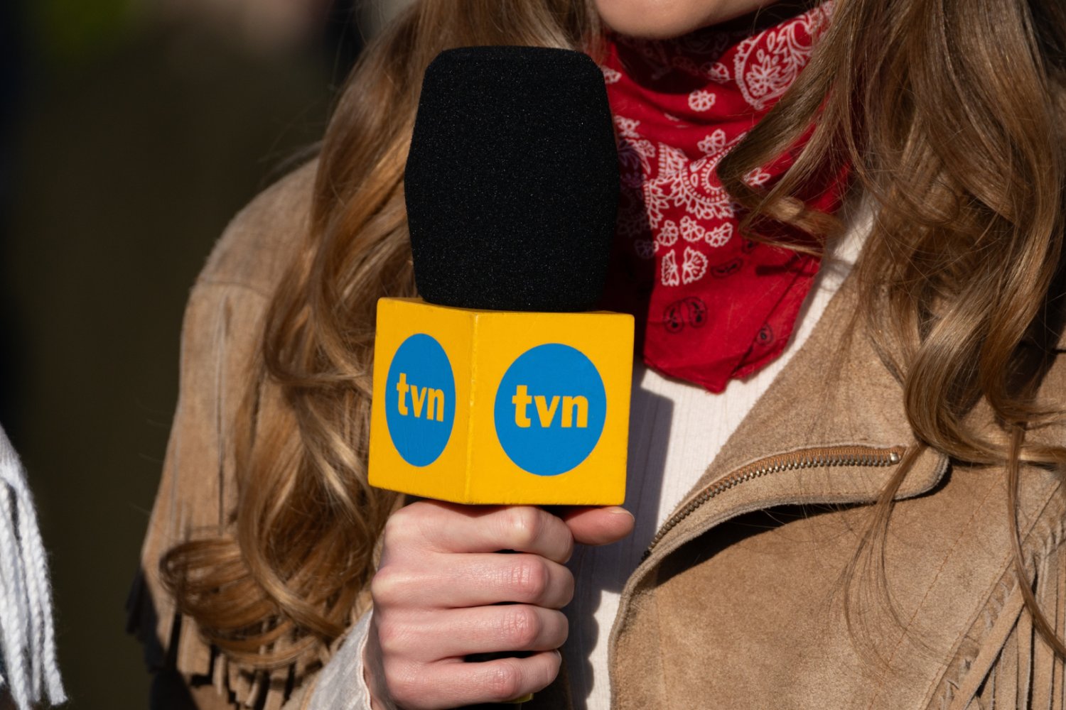 Przejęcie właściciela TVN znów wstrzymane. Znamy termin decydującej rozprawy Kobieta, dziennikarka trzymająca mikrofon z kostką z logo TVN.