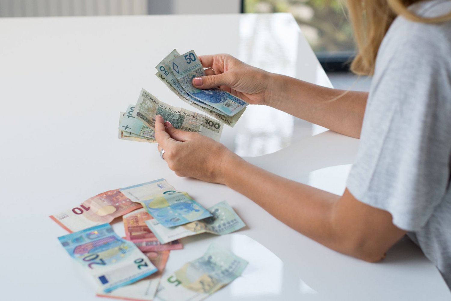 Praca i zasiłki za granicą. UE wprowadza wielkie zmiany w świadczeniach Kobieta z banknotami euro oraz polskimi złotymi. Zasiłki i praca za granicą. Wielkie zmiany w prawie UE