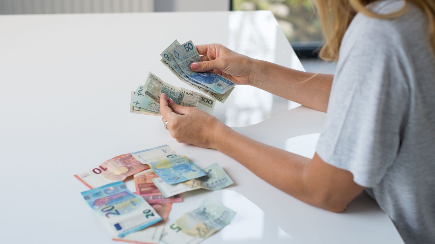 Praca i zasiłki za granicą. UE wprowadza wielkie zmiany w świadczeniach Kobieta z banknotami euro oraz polskimi złotymi. Zasiłki i praca za granicą. Wielkie zmiany w prawie UE