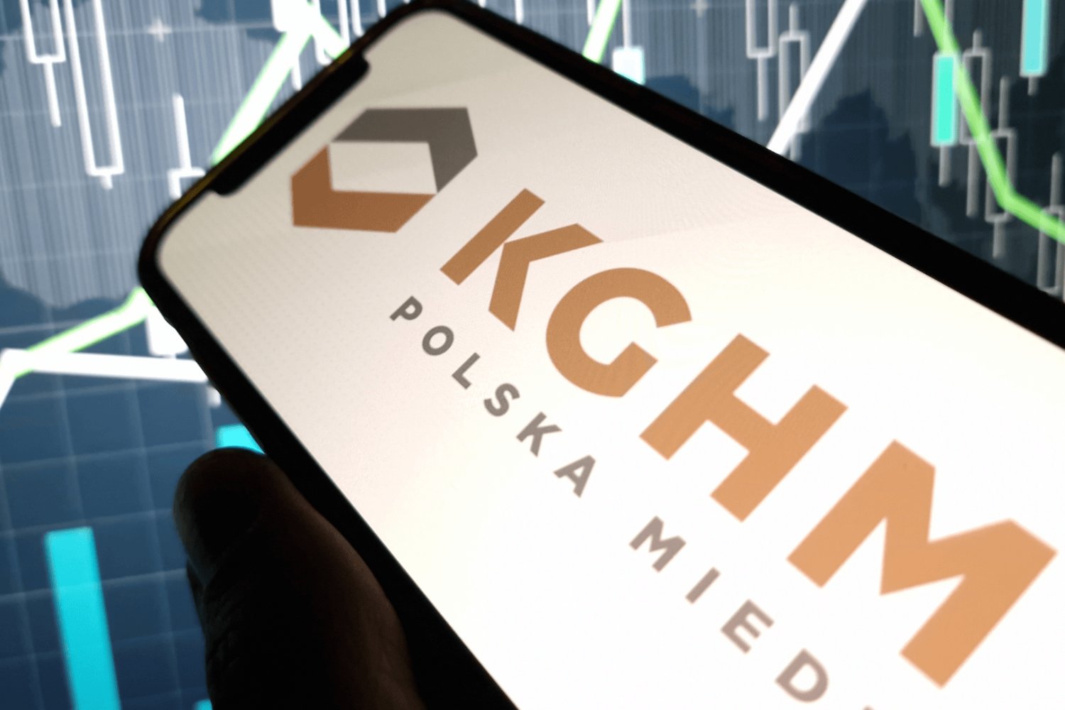 logo kghm na smartfonie, w tle świeczki giełdowe