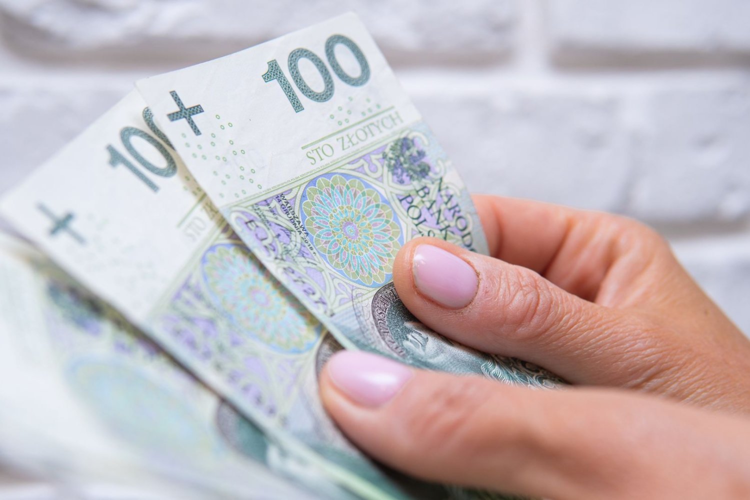 Płaca minimalna 2027. Sklepy idą na wojnę o przetrwanie. Kobieta trzyma pieniądze w dłoniach.