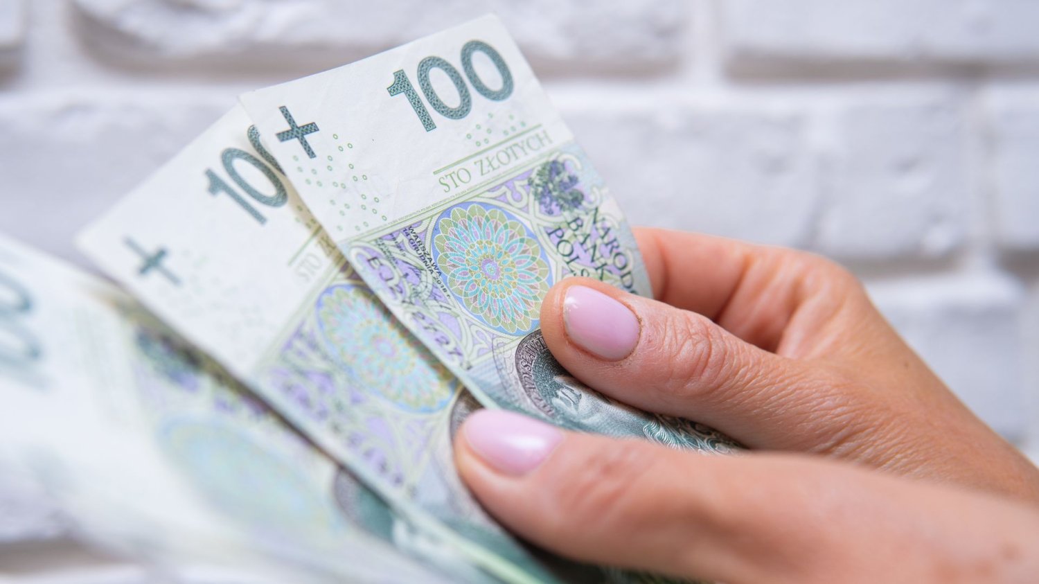 Płaca minimalna 2027. Sklepy idą na wojnę o przetrwanie. Kobieta trzyma pieniądze w dłoniach.