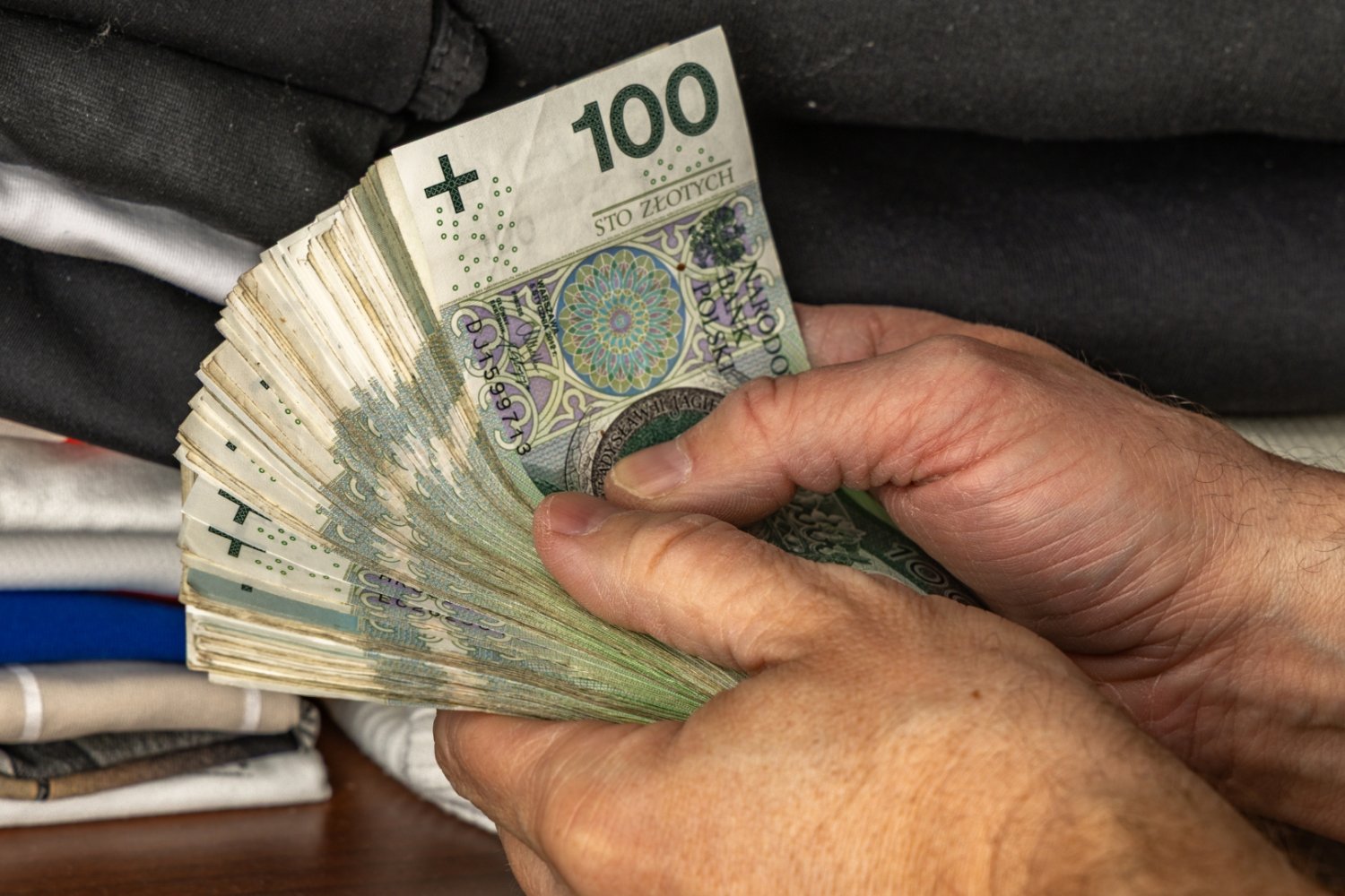 Męskie dłonie trzymające plik banknotów stuzłotowych.