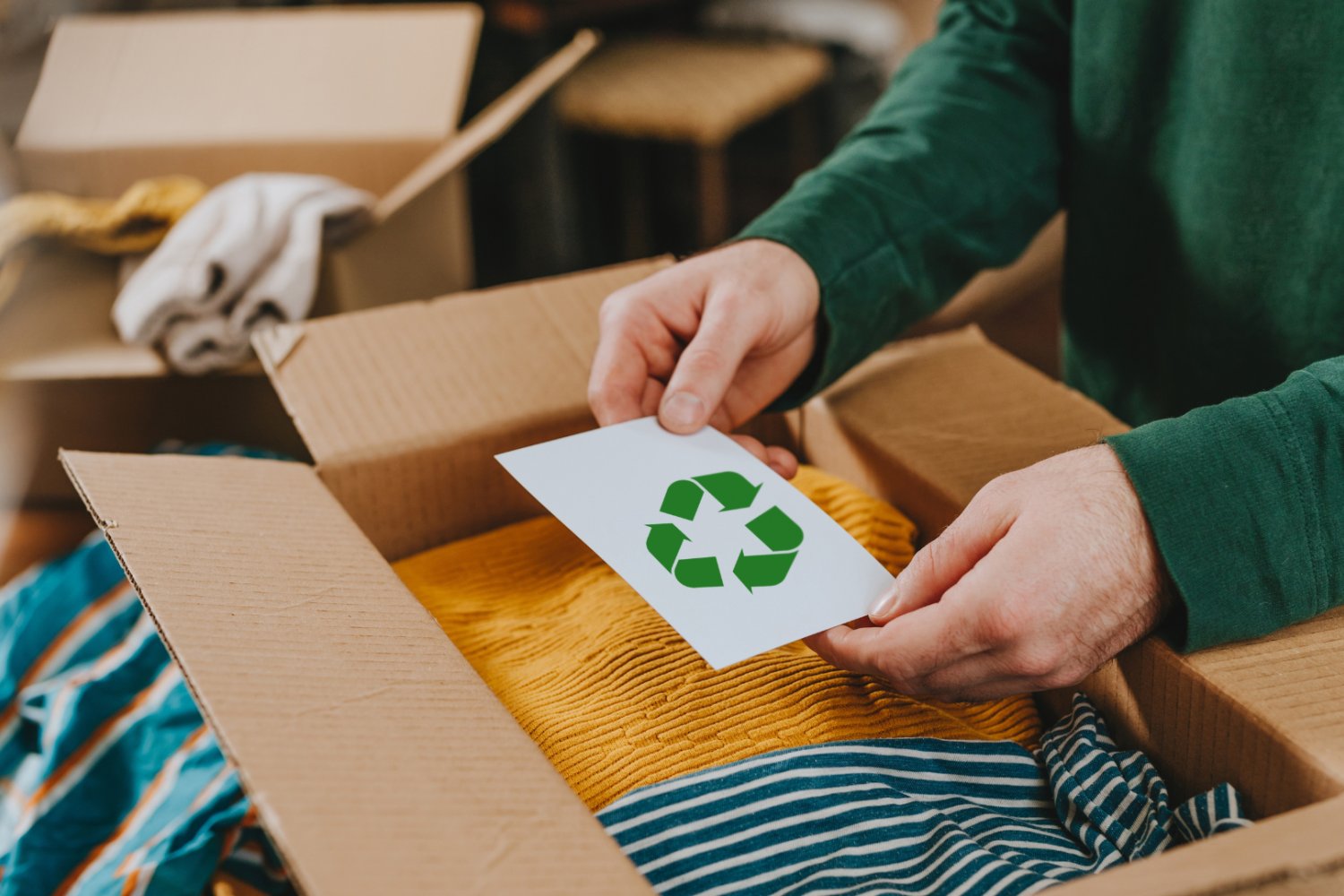 Mężczyzna trzymający kartkę nad kartonem z ubraniami. Na kartce jest znak recyklingu.