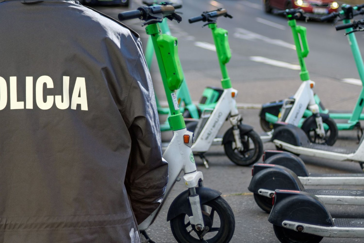 Plecy policjanta, w tle hulajnogi elektryczne.