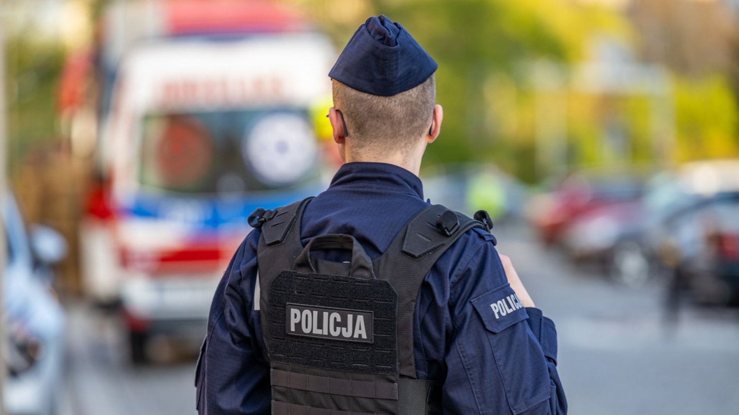 policjant od tyły, w tle ambulans.