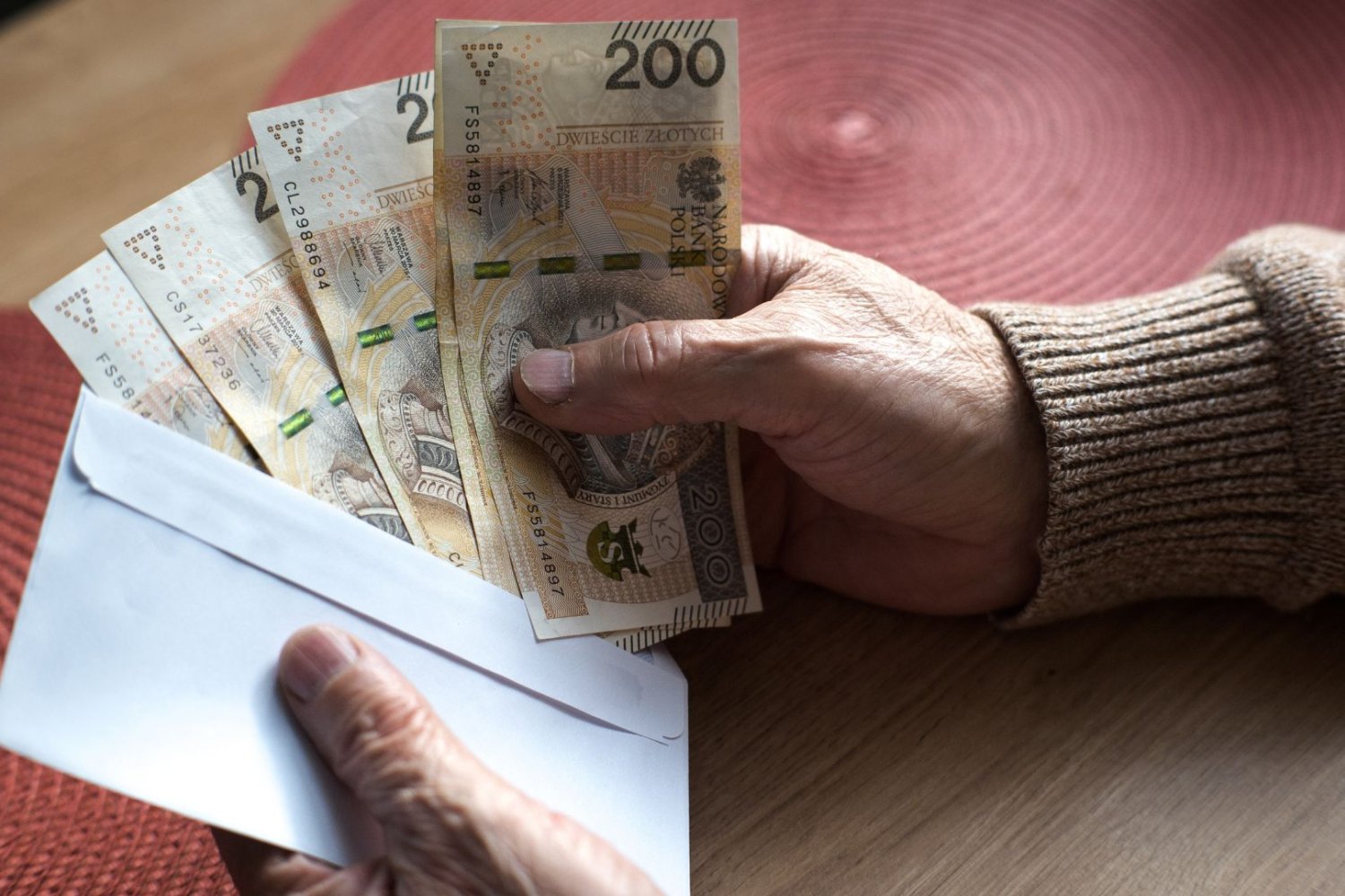 Wypłata 14. emerytury w 2026 roku. Tyle naprawdę trafi na konta. Starsza osobo trzyma w rękach kopertę z pieniędzmi.