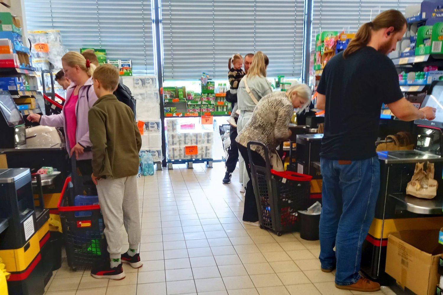 Mężczyźni i kobiety przy kasach samoobsługowych płacą za zakupy w Biedronce.
