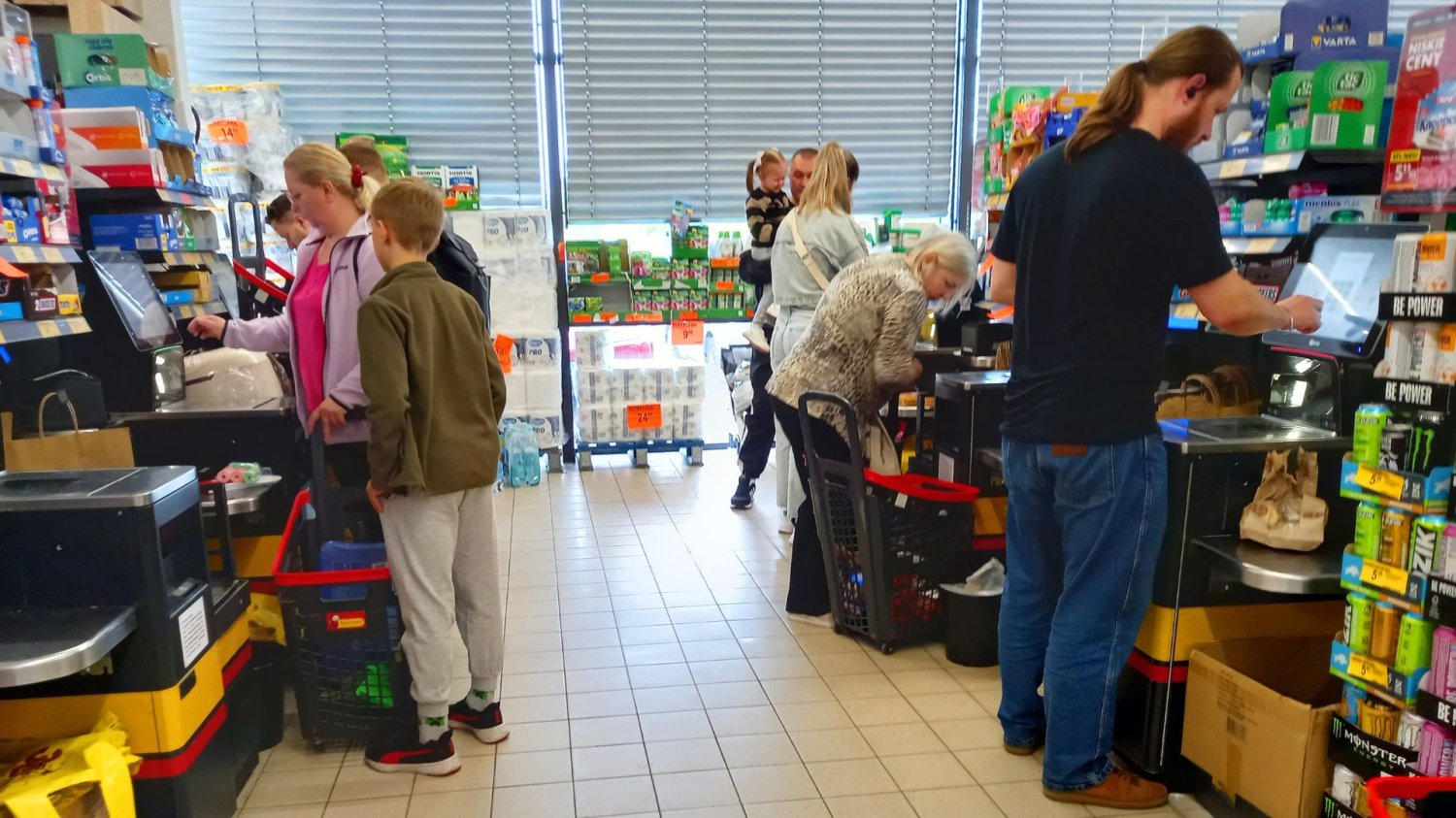 Mężczyźni i kobiety przy kasach samoobsługowych płacą za zakupy w Biedronce.