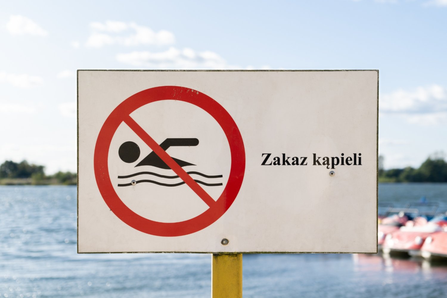 Znak "Zakaz kąpieli". W tle obiekt wodny.