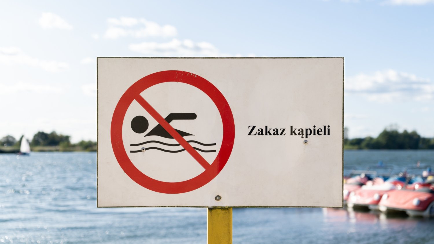 Znak "Zakaz kąpieli". W tle obiekt wodny.