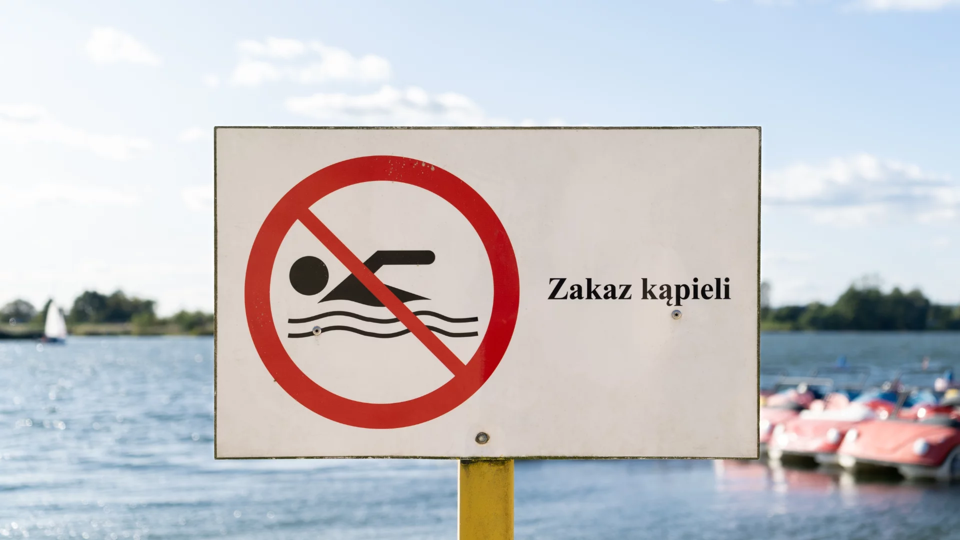 Znak "Zakaz kąpieli". W tle obiekt wodny.