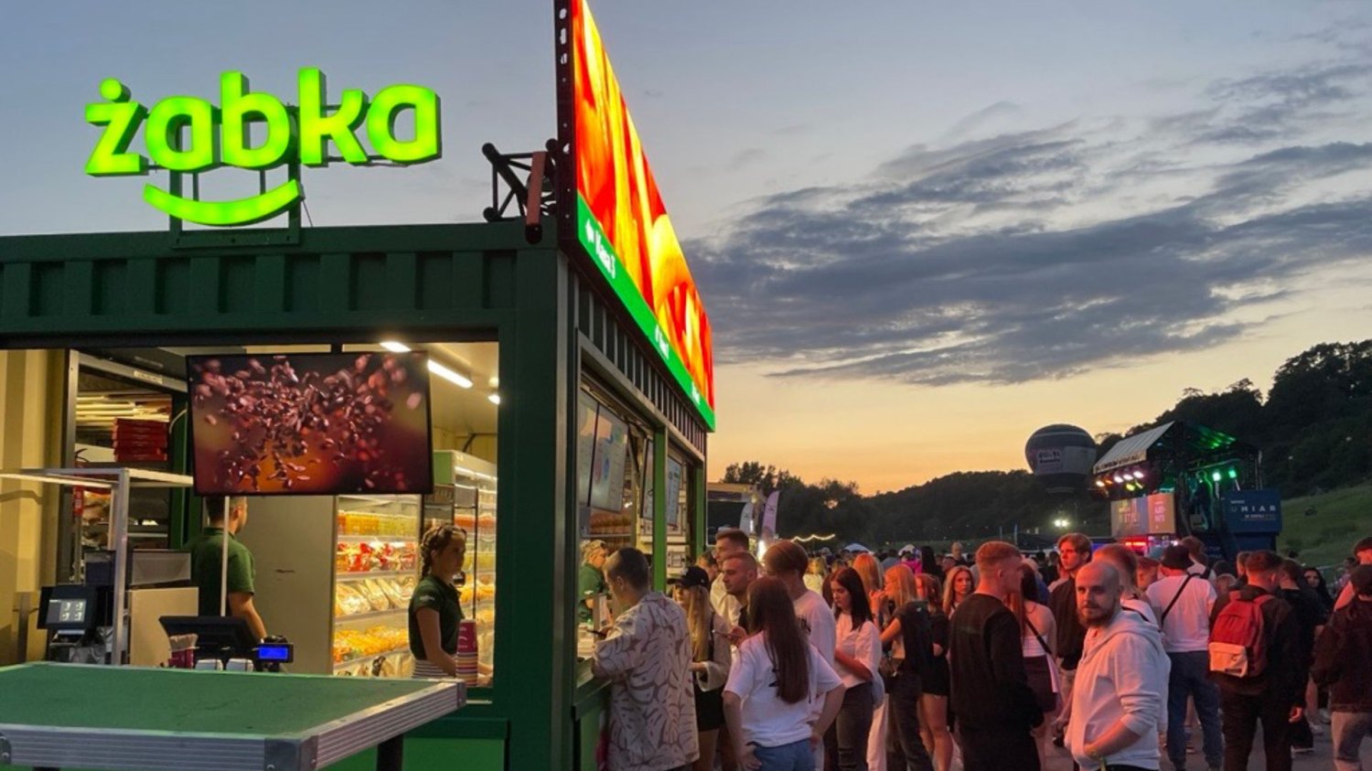 Żabka rusza w trasę koncertową. Mobilne sklepy na festiwalach. Żabka, ludzie w kolejce na festiwalu.